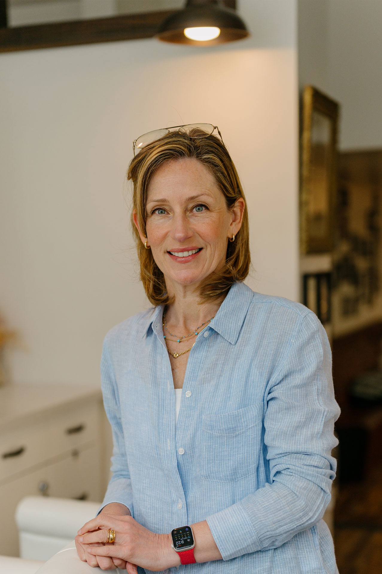 Joslyn Podesto, a hairstylist at Kosa Salon SF with glasses on her head, wearing a blue striped shirt and a smartwatch.
