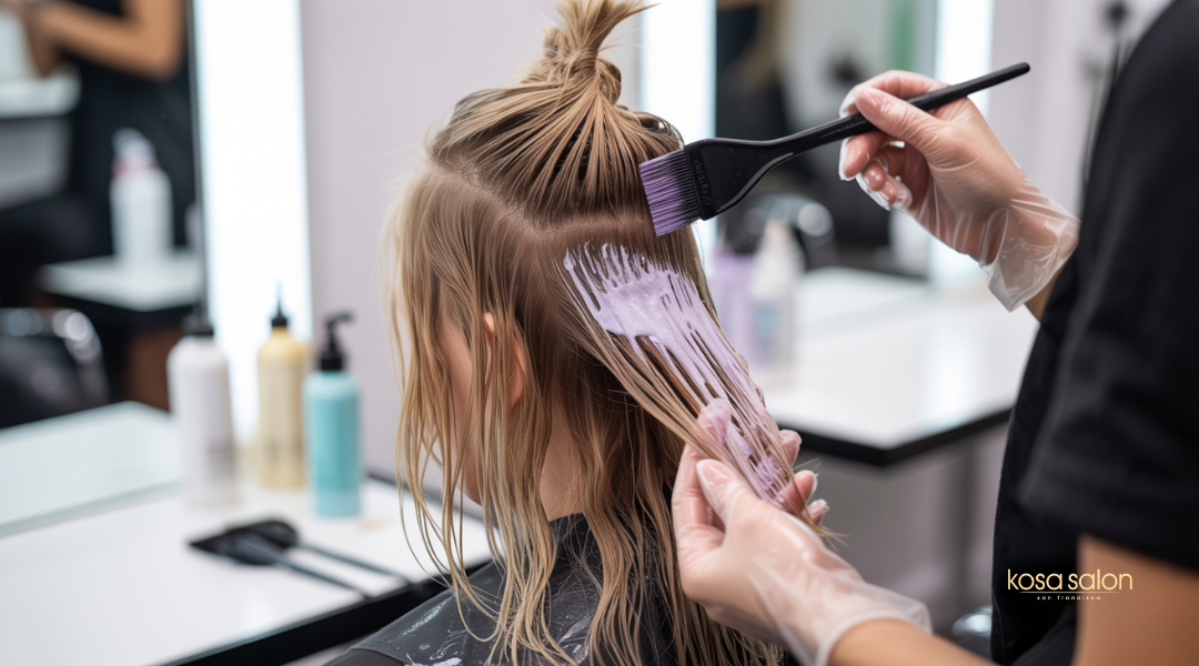 A stylist applies cool-toned hair toner to blonde hair to neutralize brassy hues, showing the transformation from warm to balanced color.

